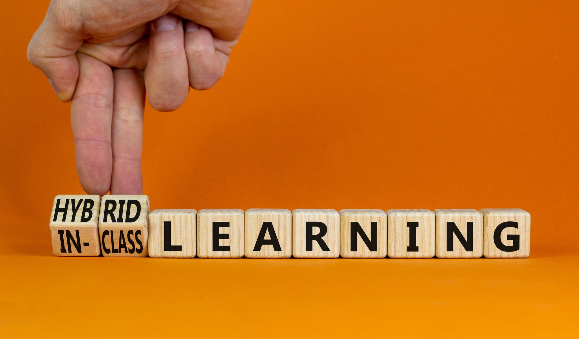 Symbole d’apprentissage hybride ou en classe. L’homme d’affaires transforme les cubes, change les mots d’apprentissage hybride en apprentissage en classe. Fond orange. Éducation et concept d’apprentissage hybride ou en classe. Espace de copie.